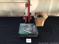 Photo showing RCBS reloading press in green box, red strut spring compressor, and cardboard box of car parts.