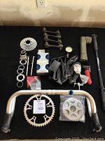 Photo of assorted bike parts laid out on black cloth including Shimano handlebars, sprockets, inner tubes, pump parts, tire pressure gauge, skewers, and linkage rods.