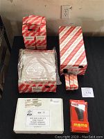 Image showing several automotive parts in original packaging on table. Includes Toyota genuine air filter, multiple oil filters in red/white boxes, white box labeled MX-T with power window control module, small red MOMO gear shift knob packaging.