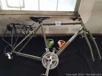 Olive drab Surly Long Haul Trucker steel frame with fork, seatpost, saddle, rack, crankset, bottle cages laid out