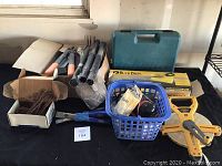 Full lot on black tablecloth showing gardening tools, coiled wire, blue basket with accessories, Buck Bros saw box, and Komelon tape measurer.