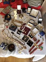 Full view of assorted costume jewelry on white cloth including multiple necklaces, several earrings in boxes, bracelets, brooches, wristwatches, and decorative items.
