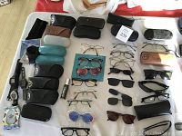 Wide view of 23 eyeglasses, sunglasses, and cases arranged on a table, showing different styles and colors.