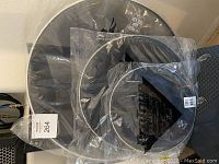 Three Pro Tone drum heads in new sealed plastic packaging, black drum heads with silver rims, arranged stacked against a wall.