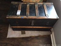 Top view of rectangular vintage black wooden trunk with natural wood metal straps and metal lock showing wear.