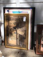 Three framed pictures stacked against a wall. Top picture shows a woman in historical dress.