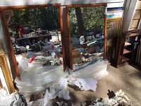 Two large wood framed rectangular mirrors placed side by side with visible wear and reflections of outdoor surroundings.