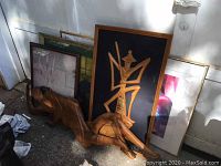Four framed pictures and three carved wooden wall decorations photographed outside near a wall.