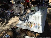 Table display of 22 assorted shot glasses and the 6-bottle liquor dispenser. Various designs on shot glasses visible, dispenser shows some black plastic stopper tops and chips on base.