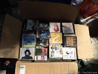 Open cardboard box filled with stacked music CDs showing album art on jewel cases.