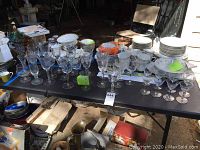 Overview of 30 pieces of mixed crystal and glass stemware arranged on a table with plates and other items in background