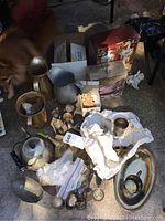 Overview of multiple metal pitchers, teapots, candle holders, and a box of liquid tea lights on a surface. Items appear aged and in need of cleaning.