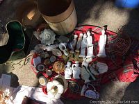 Wide view of assorted Avon milk glass perfume bottles, figurines, small vases, and other decorative items on plaid cloth and the ground.