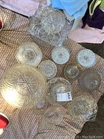 Clear glass bowls and dishes arranged on a beige textured fabric showing various intricate star and geometric patterns on bowls and dishes
