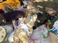 Pile of assorted linens including yellow, pastel, white pieces with embroidery and patterned fabrics on ground