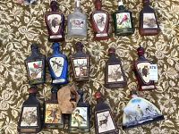Top view of 14 empty Jim Beam liquor bottles arranged on a patterned cloth, showing various wildlife designs and a ceramic Harold's Club bottle on the right
