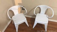 Photo of 2 white metal kids chairs from front side, showing backrest design and seats.