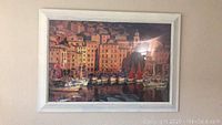 Framed art print showing a harbor scene with buildings and docked boats, taken from the front.