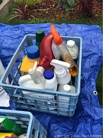 Blue plastic crate filled with various cleaning supplies including spray bottles and liquid containers.