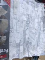 Close-up of single tile sheet showing marble pattern, glossy finish, and peel & stick branding.