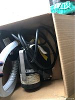 Everbilt water pump unit inside cardboard box with attached power cord and clear hoses.