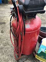 Overall front and side view of the red air compressor tank with coiled red hose and black motor cover.