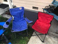 Blue and red fold-up camping chairs photographed outdoors on a concrete and grass area