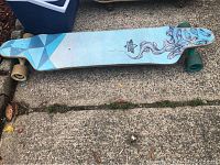 Top view of Lustice longboard showing geometric pattern with blue, turquoise, and purple abstract flowing lines on deck, green wheels visible.