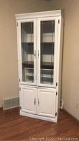 Full front view of tall white wooden cabinet with glass upper doors and solid lower doors, showing leaded decorative glass.