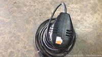 Black electric handheld sander with attached power cord placed on concrete floor.
