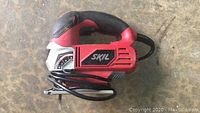 Overall view of red and black Skil skill saw with power cord folded in front.