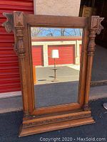 Full front view of antique wooden mirror showing carved details on the corners and base with reflective glass.