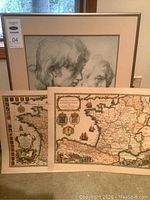 Framed Raphael print with two vintage maps displayed in front leaning against a wall.