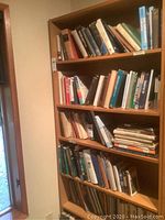 Full view of the tall wooden bookcase filled with books (not included in sale).