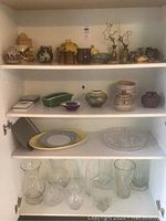 Full view of shelf with assorted ceramic vases, jars, glassware, and decorative platter