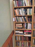 Full view of tall wooden bookshelf with multiple shelves, containing assorted books. Shows general condition and style.