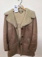 Front view of beige/tan sheepskin jacket with furry collar and two side pockets hanging on a Morlands hanger with size tag 48.