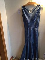 Full front view of vintage blue sleeveless dress on wooden hanger against wall