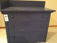 Front view of black 3-drawer chest with visible wear and round wooden knobs.