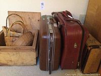 Photo showing three vintage suitcases and a wooden box containing several woven baskets.