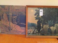Two landscape paintings, one framed and one unframed, placed side by side on wooden surface.