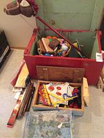 Photo showing the open vintage red wooden toy chest filled with various children's toys including a hobby horse, wooden blocks, and plastic toys with a wicker basket.