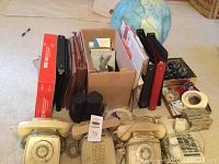 Photo showing various office supplies with folders, binders, tape, three vintage telephones, and a globe