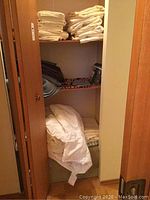 Closet with folded white and dark gray linens on shelves and white comforter at bottom.