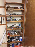 Full view of wooden shelf with mixed tools, cans, and hardware items stacked on each shelf.