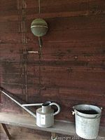 Photo of galvanized watering can and galvanized bucket on wooden shelf against rustic wood wall.