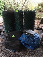 Full view showing three rolls of green plastic fencing and six assorted tarps stacked beside them