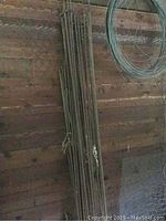Bundled steel rebar rods leaning against wooden wall with visible ribbed texture, approximately 8 feet in length.
