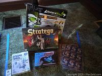 Photo showing Lot contents: Stratego game box, Lazer Tag Team Ops box, Dynamo Torch science kit, mini monster laser pegs set, and Pokemon cards.