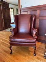Full view of brown leather wingback chair with padded arms and backrest, nailhead trim, and cabriole legs.